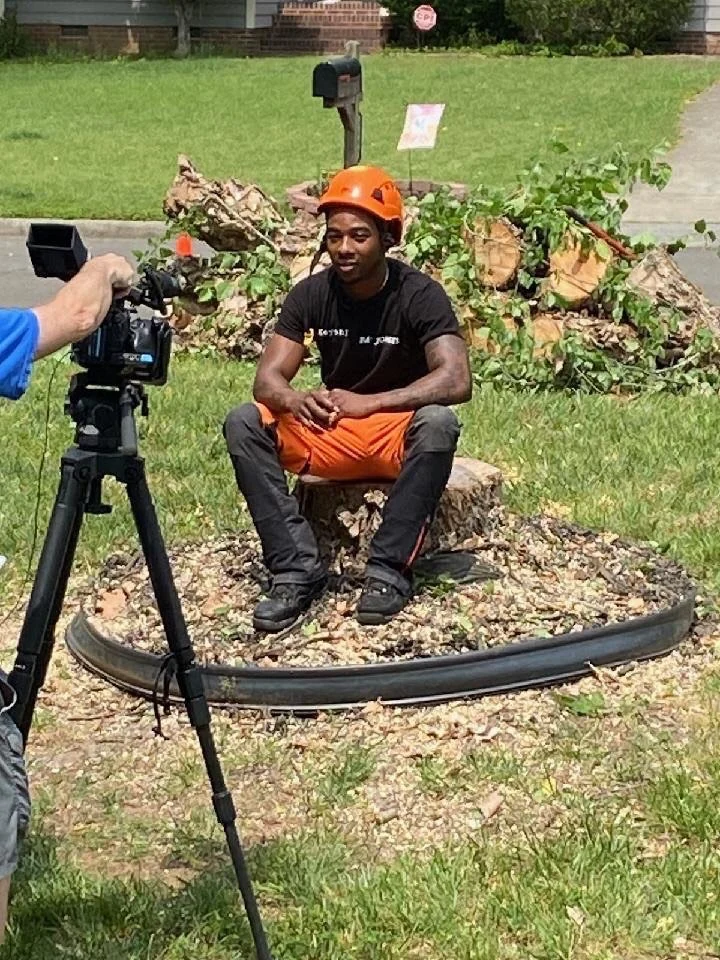 Crew member being interviewed on a job site, seated on a stump